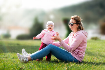 Children's day. A young mother is sitting on the grass, playing with her baby. Recreation in the park with a child. Blurred background