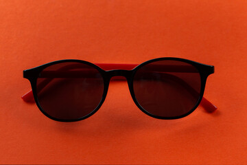 Stylish black sunglasses on an orange background folded. Fashion accessories.