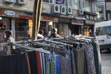 Naklejka premium A clothing rack stands outdoors for street trading. In focus, women's dresses and pants hang on the counter against the backdrop of the busy streets of Istanbul