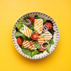 Healthy green salad with grilled halloumi cheese on yellow background, top view, space for text	