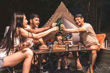 Night summer camping in the mountains, spruce forest on background..Back view group of  tourists having a rest together around campfire, enjoying fresh air near tent.