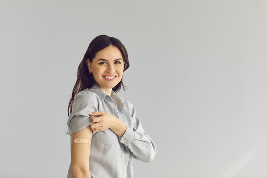 Vaccination campaign, covid coronavirus people infection prevention and protection. Young adult caucasian woman with adhesive bandage on arm studio portrait with copy space grey background
