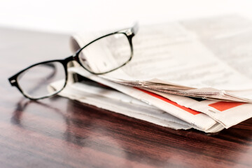 Newspaper and reading glasses on wooden table.