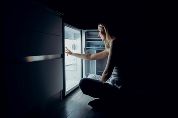 Fototapeta na wymiar Portrait of young woman opening refrigerator at night. hunger concept. the girl looks into the refrigerator.