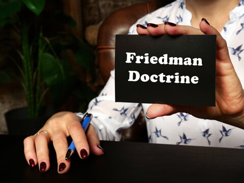 A handsome businessWoman showing a blank piece of paper with sign Friedman Doctrine . Close-up shot. Soft focus.
