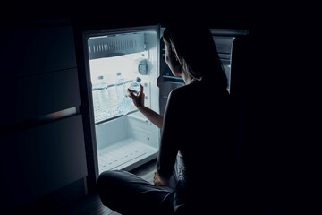 A young European woman suffers from the summer heat and lack of air conditioning at home. The girl gets fresh water from the refrigerator.