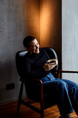 A young girl with glasses, with short hair and a nose piercing is sitting in a cafe, drinks coffee.