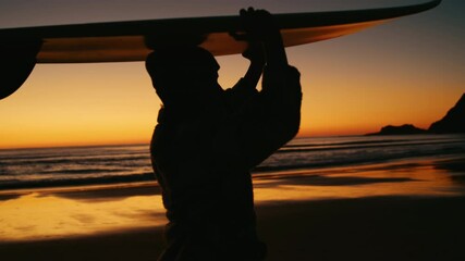 Handheld shot of professional female surfer carry surfboard back to van after long day of surfing. Last rays of sun on epic travel destination beach. Concept vanlife and surfing lifestyle