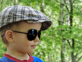A four year old boy in a checkered cap and sunglasses looks into the distance against the...