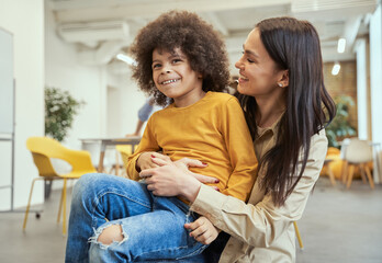 Portrait of adorable little boy with afro hair smiling, having fun together with beautiful young female teacher