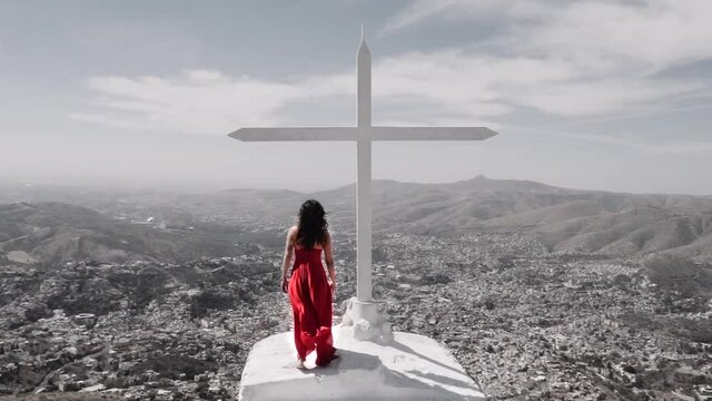 Hispanic woman wearing a red dress standing on the top of a mountain on a windy day. Slow-motion
