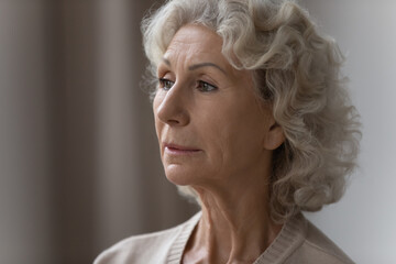 Pensive confused elderly 70s lady lost in thoughts, looking away at window. Close up portrait of senior pensioner woman forgetting things, suffering from memory loss, dementia, Alzheimer disease