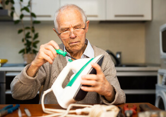 old gray haired man Repairing Iron At Table In Kitchen