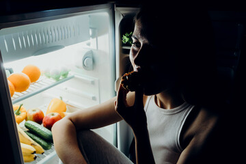 Fototapeta na wymiar Portrait of a beautiful girl taking food from the refrigerator at night. Night food, overeating concept. Diet, dieting. Beauty young woman eating dessert in refrigerator in night kitchen.