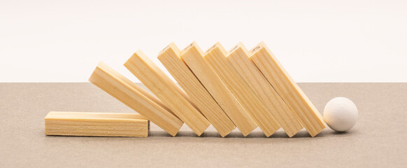 Fallen wooden blocks and a white ball on a gray background. The concept of business leadership