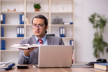 Young male employee student reading book at workplace