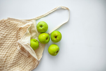 Zero waste shopping concept. Fresh vegetables in eco cotton bags on table in the kitchen. View from above on eco friendly bag filled with green organic apples, zero waste informed consumption concept