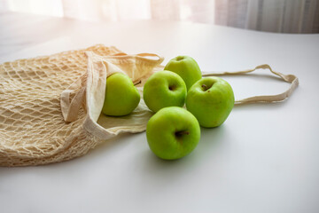 Zero waste shopping concept. Fresh vegetables in eco cotton bags on table in the kitchen. Apples in sustainable and ecological shopping bag. Zero waste consumption concept