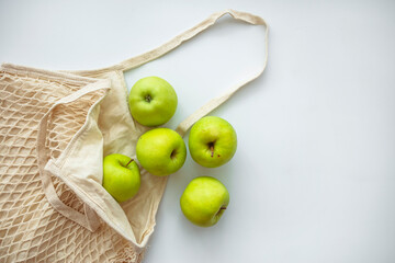 Zero waste shopping concept. Fresh vegetables in eco cotton bags on table in the kitchen. Apples in sustainable and ecological shopping bag. Zero waste consumption concept