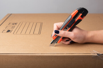 Female hand cutting with utility knife carton box