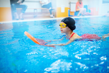 Child girl is engaged in swimming with trainer in pool, uses polyurethane stick to practice stroke