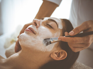 Beautiful brunette woman enjoying applying cosmetic mask with closed eyes comfortable and blissful. Relaxing treatment in medicine and spa center concepts