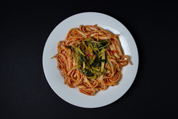 Spaghetti in tomato sauce on a dark background. Spaghetti with a vegetable side dish on a black background. Italian food. Tasty food