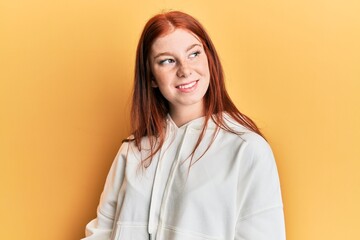 Young red head girl wearing casual sweatshirt looking away to side with smile on face, natural expression. laughing confident.