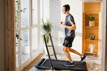Young man jogging on the modern compact treadmill at his home