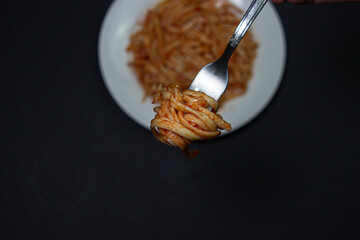 Spaghetti in tomato sauce on a dark background. Spaghetti fork on a black background. Italian food. Tasty food