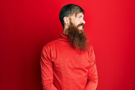 Redhead man with long beard wearing casual clothes looking to side, relax profile pose with natural face and confident smile.