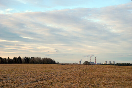 Early spring landscape of feald and sky with chimneys of thermal power plant in the distance with clouds of steam. Ecological problem  