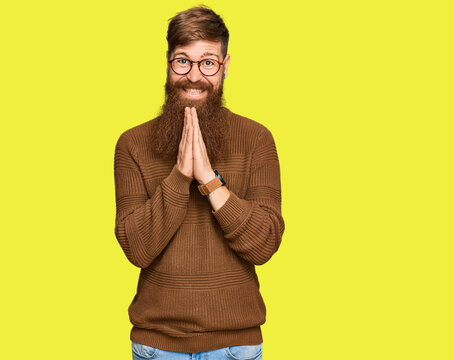 Young irish redhead man wearing casual clothes and glasses praying with hands together asking for forgiveness smiling confident.