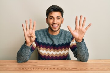 Young handsome man wearing casual sweater sitting on the table showing and pointing up with fingers...