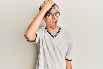 Young hispanic man wearing casual clothes and glasses surprised with hand on head for mistake,...