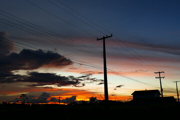 Fototapeta na wymiar Colorful tropical sunset, power poles strung together with wires along a straight long road. Rorainópolis, state of Roraima, Brazil.