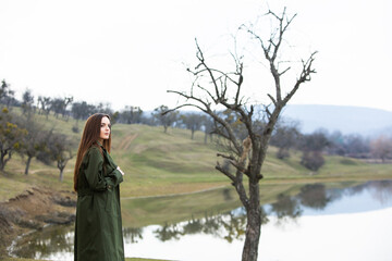 Image of young beautiful woman wearing rain jacket in cold weather. Thinker european girl in spring nature.
