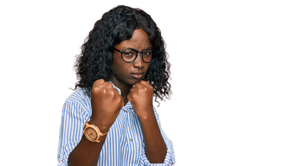 Fototapeta na wymiar Beautiful african young woman wearing casual clothes and glasses ready to fight with fist defense gesture, angry and upset face, afraid of problem