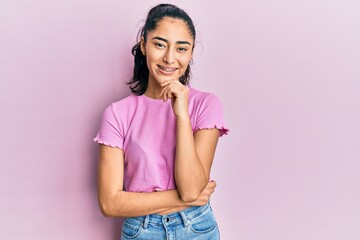 Hispanic teenager girl with dental braces wearing casual clothes smiling looking confident at the camera with crossed arms and hand on chin. thinking positive.