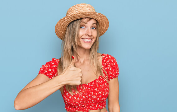 Beautiful caucasian woman wearing summer hat doing happy thumbs up gesture with hand. approving expression looking at the camera showing success.