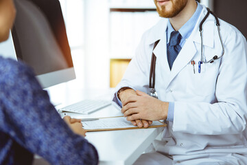 Unknown bearded doctor and patient woman discussing current health examination while sitting in...
