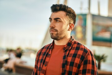 Young hispanic man with serious expression standing at the city.