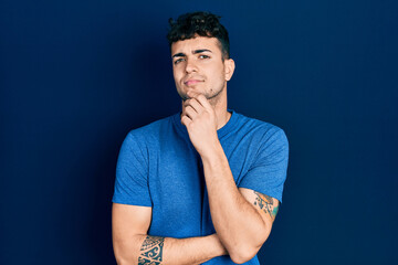 Young hispanic man wearing casual clothes thinking concentrated about doubt with finger on chin and...