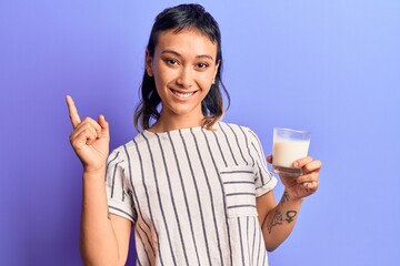 Young woman holding glass of milk smiling happy pointing with hand and finger to the side
