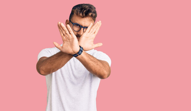 Young hispanic man wearing casual clothes and glasses rejection expression crossing arms doing negative sign, angry face