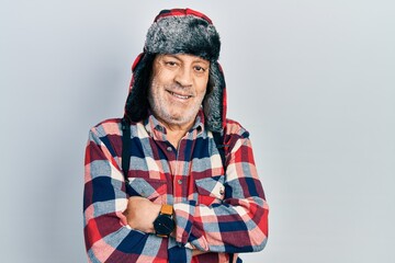 Handsome mature man wearing winter hat with ear flaps happy face smiling with crossed arms looking at the camera. positive person.