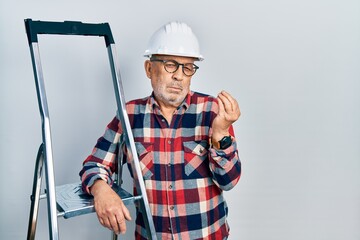 Handsome mature handyman close to construction stairs wearing hardhat doing italian gesture with hand and fingers confident expression
