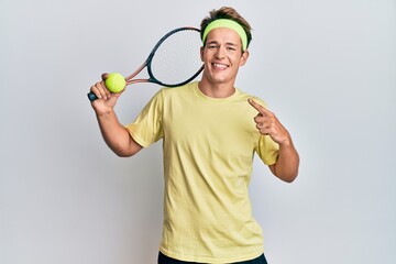 Handsome caucasian man playing tennis holding racket and ball smiling happy pointing with hand and finger