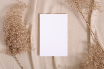 White blank paper card mockup with pampas dry grass on a beige neutral colored textile