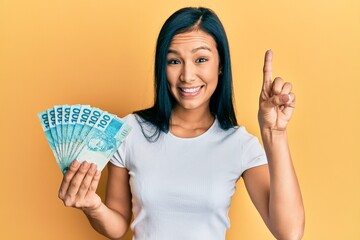 Beautiful hispanic woman holding 100 brazilian real banknotes smiling with an idea or question...